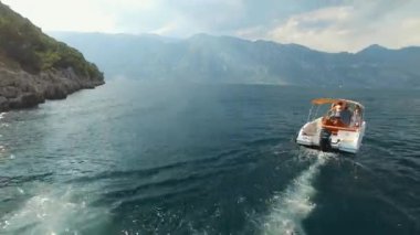 Bir turist teknesi Kotor Körfezi 'nin ortasında yelken açıyor. Önünde bir yelkenli yatı var.