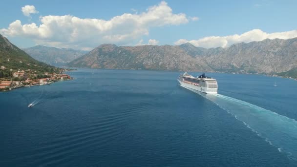 The cruise ship sails along the Bay of Kotor, behind it there are beautiful mountains and cozy little town near it. — Stock Video