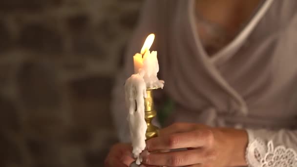 Μια γυναίκα με μεταξωτή ρόμπα κρατά αναμμένο κερί. — Αρχείο Βίντεο