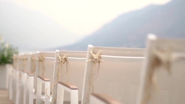 White wedding venue with decorated white chairs against the mountains — Vídeos de Stock