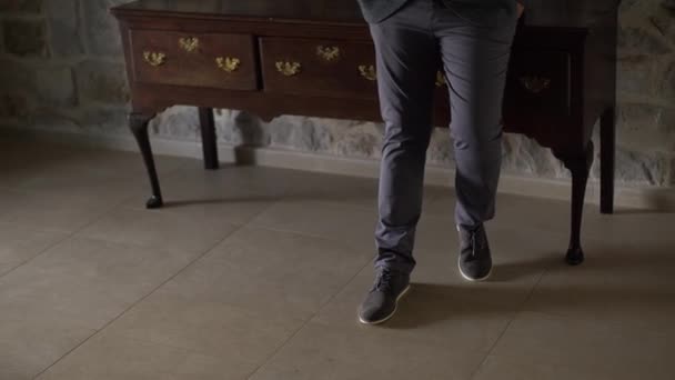Nogi mężczyzny stojącego w pokoju obok eleganckiej, długiej szafki, zbliżenie — Wideo stockowe