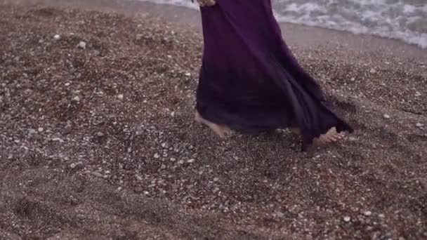 穿着紫色长裙的赤脚女人沿着卵石滩散步 — 图库视频影像