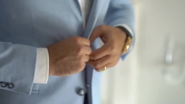 Bir adam hazırlanıyor ve ceketinin düğmelerini ilikliyor.