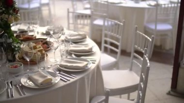 Düğün yemeğinde bir buket çiçek ve zarif beyaz sandalyelerle süslenmiş servis masası.