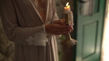 İpek bornozlu bir kadın yanan bir mum tutuyor.