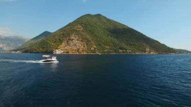 Bir turist teknesi Kotor Körfezi 'nin ortasında yelken açıyor. Önünde bir yelkenli yatı var.