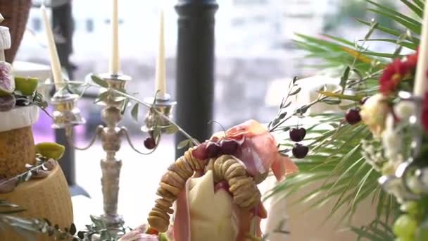 A festive snack at a wedding banquet - heads of cheese, prosciutto, figs, cherries, a candelabrum with candles next to them — Vídeos de Stock