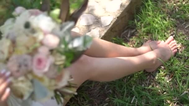 Kaki seorang gadis dalam sebuah peignoir anggun, duduk di jalan dengan buket pengantin di tangannya — Stok Video