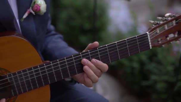 En man i kostym med boutonniere spelar akustisk gitarr — Stockvideo