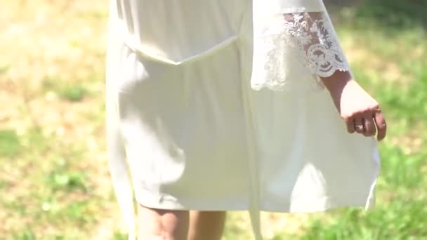 Rückansicht einer Frau in einem anmutigen Peignoir, die an einem Sommertag auf einem Gras spaziert — Stockvideo