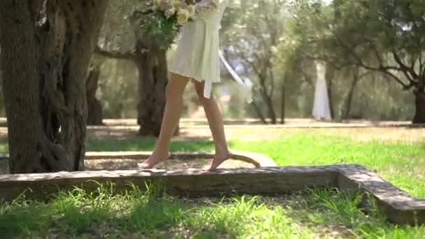 Bosá dívka v krátkých šatech chodí po trávě a drží svatební kytice, zblízka