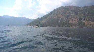 Yelkenli yat Kotor Körfezi boyunca ilerliyor. Arkasında güzel dağlar var. 