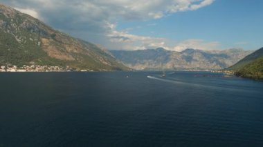 Bir turist teknesi Kotor Körfezi 'nin ortasında yelken açar. Önünde bir dağ ve rahat bir kasaba vardır.