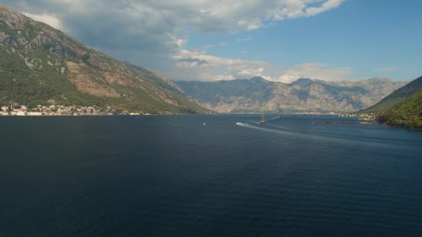 Een toeristische boot vaart in het midden van de baai van Kotor, voor het is een berg en gezellige stad — Stockvideo