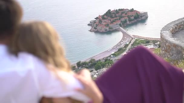 Le couple est assis dans ses bras et regarde d'en haut sur l'île de Sveti Stefan — Video
