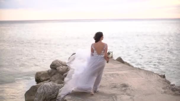 新娘带着结婚花束沿着码头走着，裙子在风中飘扬 — 图库视频影像