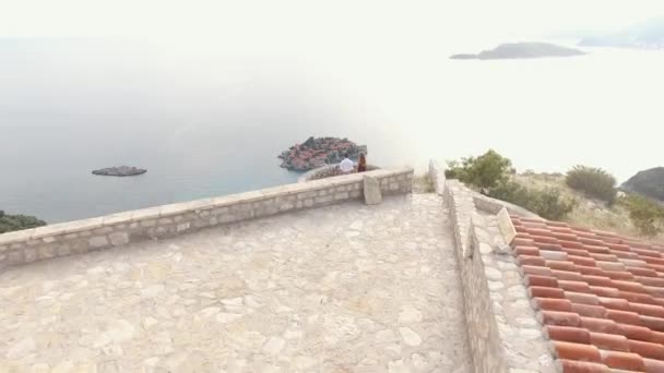 Sveti Stefan adasına bakan eski kilisenin yanındaki gözlem güvertesinde bir çift. — Stok video