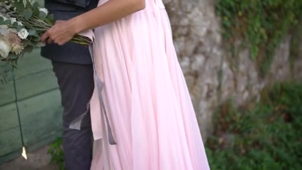 El novio abraza a la novia en un hermoso vestido con la espalda abierta, la novia tiene un ramo en la mano — Vídeo de stock