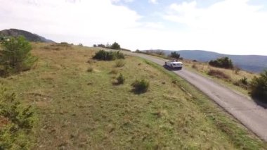 Üstü açık beyaz bir araba Lovcen Dağı 'nda yol boyunca gidiyor.