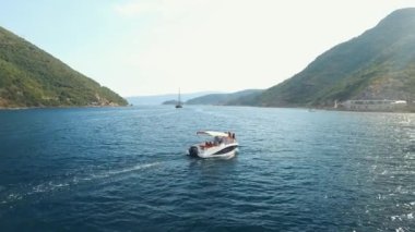 Bir turist teknesi Kotor Körfezi 'nin ortasında yelken açıyor. Önünde bir yelkenli yatı var.