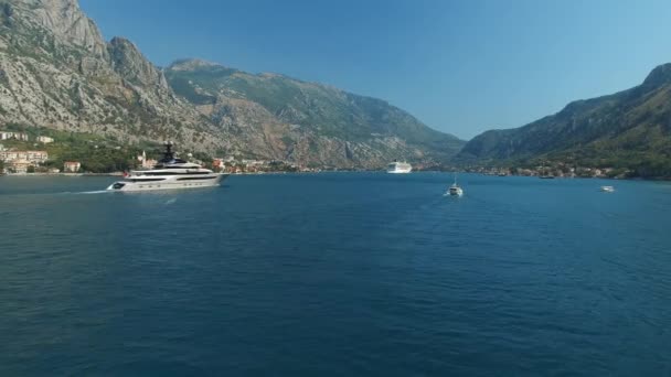Jacht płynie wzdłuż Zatoki Kotor, za nim są piękne góry i przytulne miasteczko — Wideo stockowe