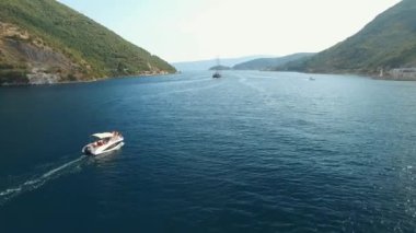 Bir turist teknesi Kotor Körfezi 'nin ortasında yelken açıyor. Önünde bir yelkenli yatı var.