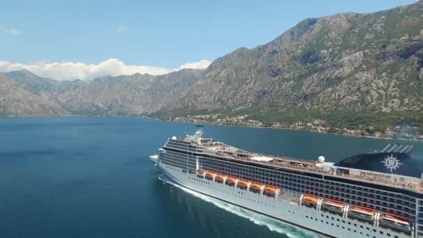 La nave da crociera naviga lungo la baia di Kotor, dietro di essa ci sono bellissime montagne, i ciottoli sono visibili nell'acqua limpida, vista aerea — Video Stock