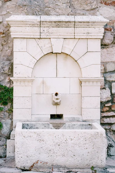 Uma fonte de bebida de azulejos com uma tigela de pedra em uma parede de paralelepípedos. — Fotografia de Stock