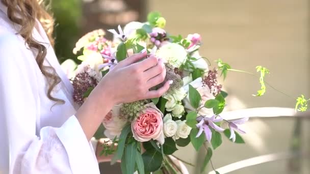 Seorang gadis di sebuah peignoir dengan rambut mengalir memegang buket pernikahan di tangannya — Stok Video
