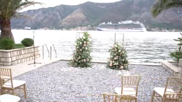 Miejsce ślubu nad brzegiem Zatoki Kotorskiej, łuk ozdobiony kwiatami i żaglami statku w oddali — Wideo stockowe