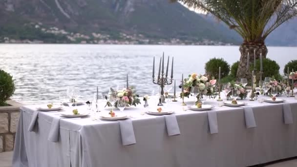Ein Tisch bei einem Hochzeitsbankett, geschmückt mit Blumen, Kerzenständern und jungen Granatäpfeln auf der Seebrücke in der Bucht von Kotor — Stockvideo