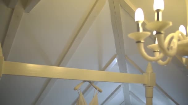 Delikat brudekjole hænger på en stråle ved siden af arbejder lysekrone i hotelværelset – Stock-video