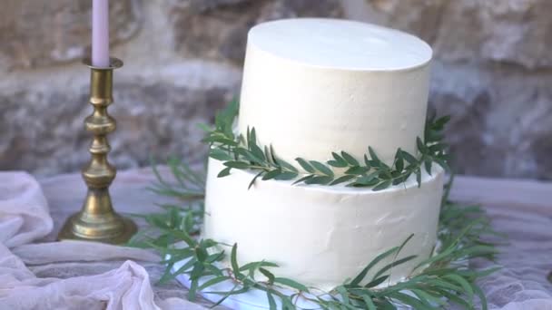Białe ciasto kremowe, ozdobione gałązkami oliwnymi i eukaliptusowymi, obok świec w złotych świecznikach — Wideo stockowe