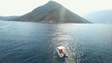 Bir turist teknesi Kotor Körfezi 'nin ortasında yelken açar. Önünde bir dağ ve rahat bir kasaba vardır.