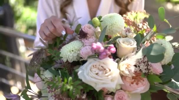 Una ragazza in un peignoir con i capelli fluenti tiene in mano un bouquet da sposa — Video Stock