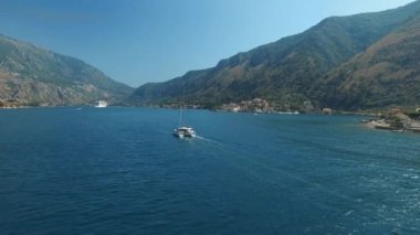 Küçük yatlar Kotor Körfezi boyunca yelken açıyor. Arkasında güzel dağlar ve rahat küçük bir kasaba var.