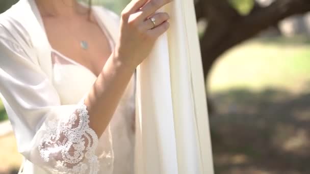 Mireasa într-un peignoir atinge rochia ei de mireasă, care alunecă pe un copac — Videoclip de stoc