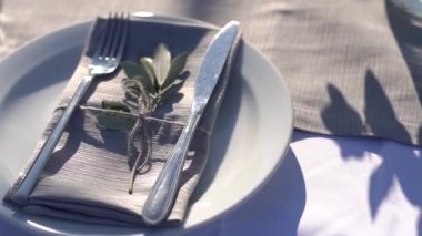 Tabak, çatal bıçak ve peçete festival masasında, zeytin filizi ile süslenmiş.