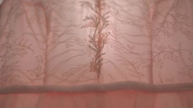 Girişte asılı soluk pembe bir gelinliğin boncuklu korsesi, yakın plan.
