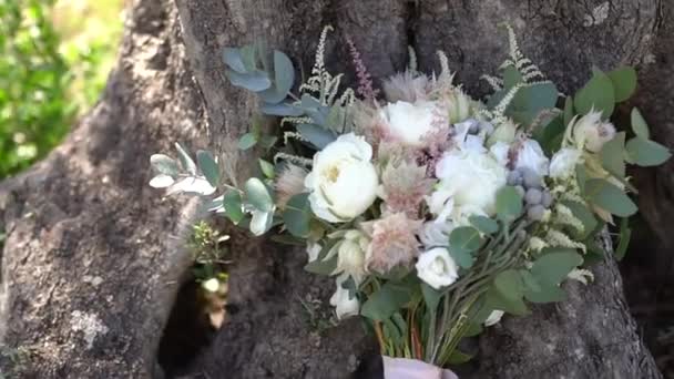 Delicaat bruidsboeket van rozen, lisianthus, astilba en eucalyptus takken ligt op de grond in de buurt van een boomstam — Stockvideo