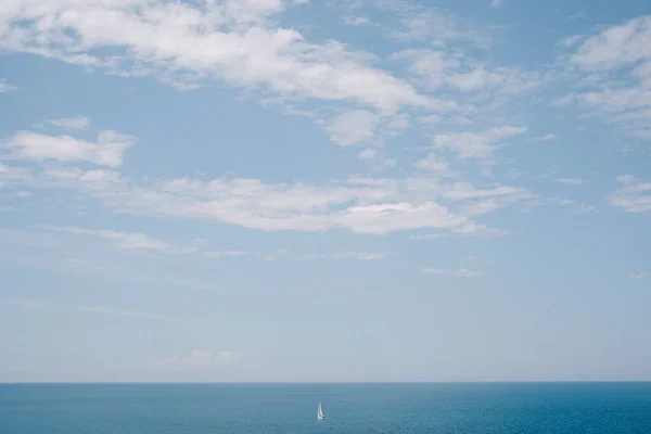 Одинокий парусник плавает вдалеке на спокойной воде на фоне голубого неба. Понятие свободы и легкости. Синий летний фон. — стоковое фото
