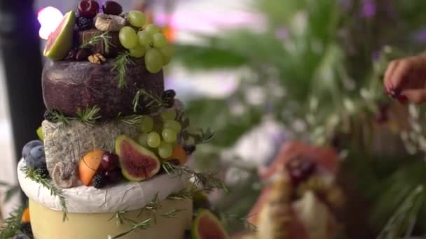 A womans hand puts a berry on the cheese head cake snack, fruits, nuts and greens at the wedding buffet — Stock Video