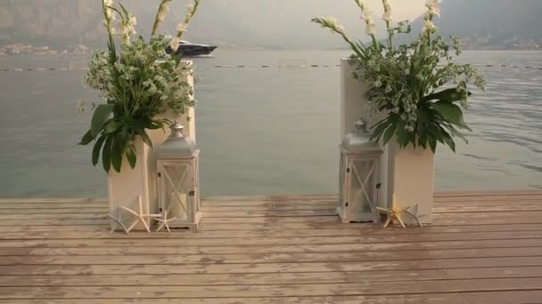 Wedding arch on the pier against the background of the sea and mountains - bouquets, starfish and decorative lanterns — Stock Video