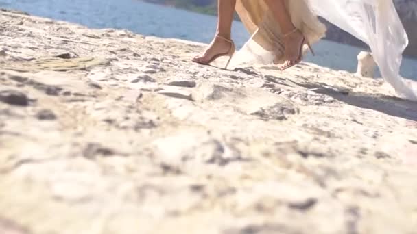 Una novia con un vestido blanco camina por el muelle, sus faldas revoloteando en el viento — Vídeos de Stock