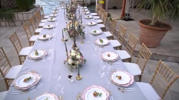 Een tafel op een bruiloft banket, versierd met bloemen, kandelaars met brandende kaarsen en jonge granaatappels op de pier aan zee — Stockvideo