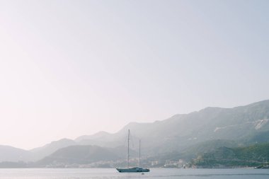 Sisli bir yaz sabahında, dağların arka planında bir yat.