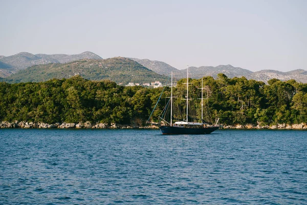 Beautiful three-masted wooden ship off the coast of Croatia. A large wooden yacht is moored along the rocky coast and forest.