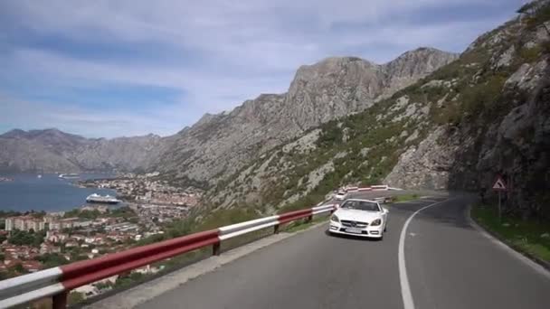 Bílý kabriolet jede po silnici na hoře Lovcen na pozadí malebného výhledu na záliv Kotor — Stock video