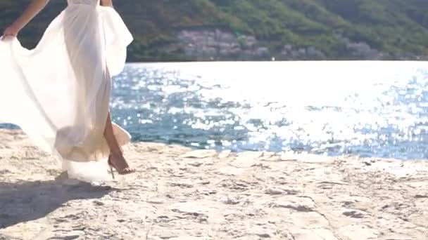 Beyaz elbiseli bir gelin iskelede yürüyor, etekleri rüzgarda dalgalanıyor. — Stok video