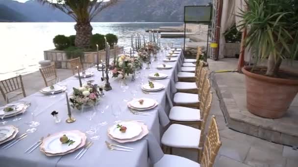 Τραπέζι σε γαμήλιο δείπνο, διακοσμημένο με λουλούδια, κηροπήγια και νεαρά ρόδια στην προβλήτα του κόλπου του Κότορ — Αρχείο Βίντεο